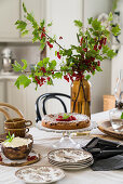 Johannisbeerzweige in der Vase auf gedecktem Tisch mit Kuchen