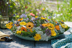 Wreath of marigolds, yarrow, sage, oregano flowers and sweet peas as table decoration