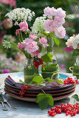 Kleine Sträuße aus Rosenblüten und großer Bibernelle in Flaschen als Tischdeko, rote Johannisbeeren