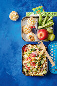 Sushi-Reisbällchen, Gemüse, Obst und Nudelsalat in Lunchboxen