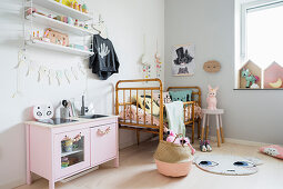 Pink play kitchen next to cot in girl's bedroom in pastel shades
