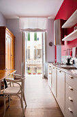 Blick durch langgestreckte Küche in Kleinwohnung mit weißer Küchenzeile vor roter Wand