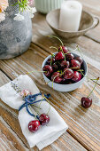 A candle, a vase, a bowl of cherries and fabric napkins on a wooden table