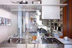 View over stainless steel kitchen island through glass walls into living area with sofa and fitted cabinets