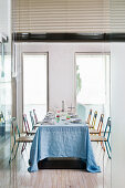 Long dining table set for 8 with blue tablecloth and colourful steel-tube chairs
