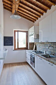 Kitchen with white cupboards and exposed wooden roof structure in Tuscan country house