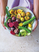 Hands holding a bowl of mini zucchini, figs, patissons and beetroot