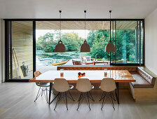 Dining table, shell chairs and corner bench next to glass wall