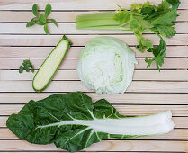 Flatlay of nutritious green herbs and vegetables arranged on a wooden background