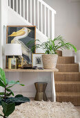 Pictures, lamp and houseplant on table next to foot of stairs