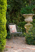 Romantischer Gartenplatz mit Metallstuhl neben bepflanzter Amphore