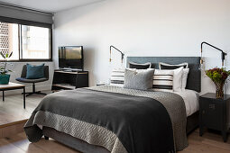 Grey double bed and seating area on platform in studio apartment