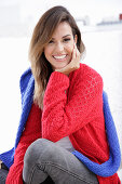 A young woman wearing a red knitted jumper with a blue jumper over her shoulders