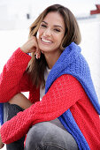 A young woman wearing a red knitted jumper with a blue jumper over her shoulders