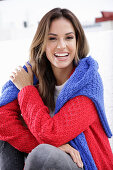 A young woman wearing a red knitted jumper with a blue jumper over her shoulders