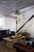 Rustic coffee table and sofa in interior with staircase and silver stucco ceiling