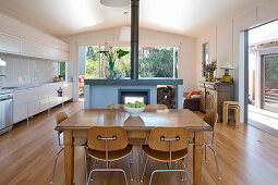 Dining table, chairs and fireplace next to white kitchen counter in open-plan interior