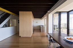 Dining table and metal chairs next to terrace doors and kitchen in open-plan interior