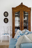 Hellblaues Sofa mit Kissen, antiker Vitrinenschrank und Stuhl im Wohnzimmer
