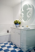 Washstand below round mirror in bathroom with blue-and-white floor tiles