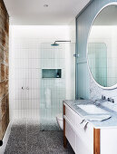 Round mirror above vanity with marble top in bathroom with shower area