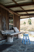Holzbank und Hocker auf überdachter Terrasse einer rustikalen Holzhütte