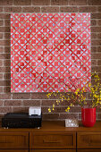 Red geometric artwork on brick wall above wooden chest of drawers