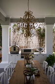Decorative chandelier above wooden dining table on roofed terrace with pillars
