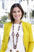 A young woman wearing a chunky necklace, a white jumper and a yellow bouclé jacket