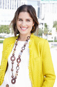 A young woman wearing a chunky necklace, a white jumper and a yellow bouclé jacket