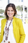 A young woman wearing a chunky necklace, a white jumper and a yellow bouclé jacket
