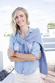 A blonde woman wearing a denim shirt with a jumper over her shoulders