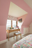 Desk below window in attic bedroom with pink walls