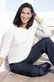 A brunette woman wearing a white jumper and polka dot trousers