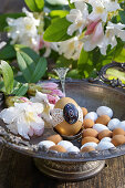 Egg with tip in a silver bowl with rhododendron flowers and marzipan eggs