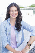 A young woman wearing a purple t-shirt, a denim shirt and white trousers