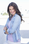 A young woman wearing a purple t-shirt, a denim shirt and white trousers