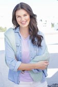 A young woman wearing a purple t-shirt and a denim shirt with a jumper over her shoulders