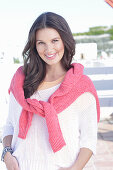 A young woman wearing a white summer jumper and a fuchsia-coloured jumper over her shoulders