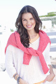 A young woman wearing a white summer jumper and a fuchsia-coloured jumper over her shoulders