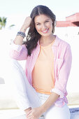 A young woman wearing an apricot top, a pink striped shirt and white trousers