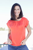 A mature brunette woman wearing a red blouse and jeans