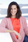 A mature brunette woman wearing a red blouse and a wrap-around jumper