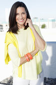 A mature brunette woman wearing a yellow top with a jumper over her shoulders