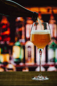 Beer in wineglass with foam on wooden counter in bar on blur background