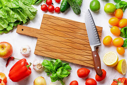 Frisches Gemüse, Blattsalat und Obst um ein Holzschneidebrett mit Messer
