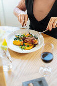 Frau isst Kalbssteak auf Kürbis-Spinat-Salat mit Mango