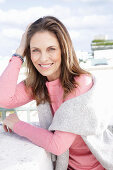 A long-haired woman wearing a pink top with a grey jumper over her shoulders