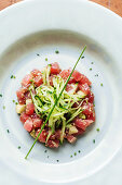 Pieces of red tuna served with slices of cucumber and herbs on white plate