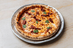 Baked pizza served with cheese, herbs and dried tomato on table